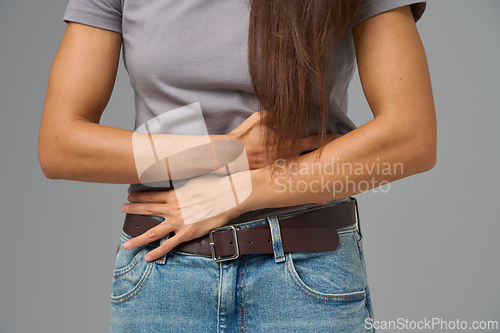 Image of Close-up of woman s hands clutching stomach in pain, studio shot on neutral grey