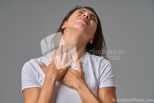 Image of Woman touching chest and neck with eyes closed showing discomfort or sore throat indoors