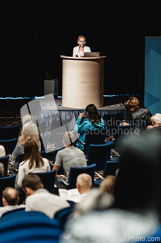 Image of Female speaker giving a talk on corporate business conference. Unrecognizable people in audience at conference hall. Business and Entrepreneurship event.
