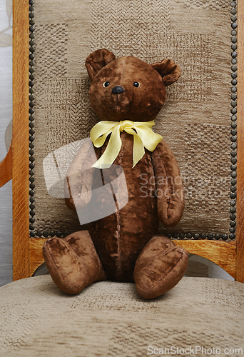 Image of shabby teddy bear with a yellow bow on his neck sitting in an ol