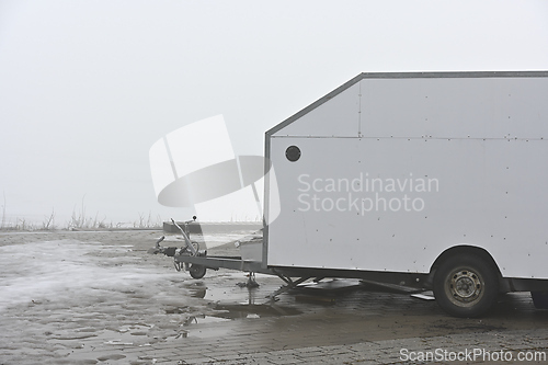 Image of deadpan photo of a white trailer on the shore of a lake in the h