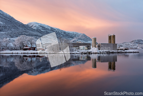 Image of Snow-covered factory by the lake with a vibrant sunset in a moun