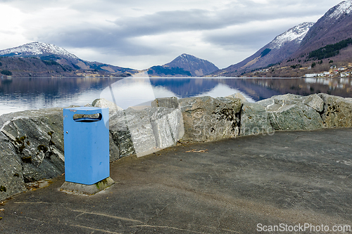 Image of Lakeside view with a blue trash bin near a rocky shoreline and m