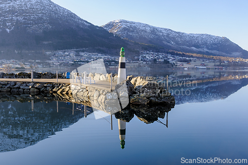 Image of Scenic pier with lighthouse at dawn reflecting in still water wi