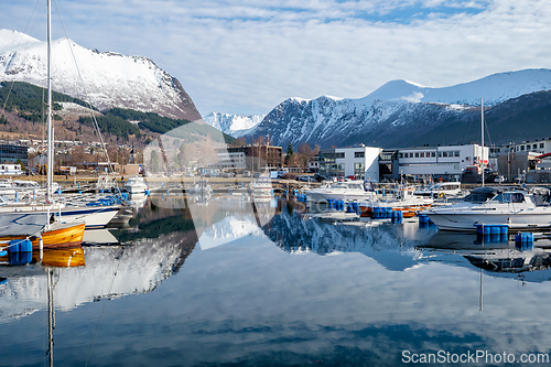 Image of Scenic view of a marina with boats on calm water and mountains i