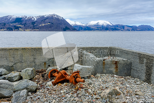 Image of Rusty equipment sits on rocky shore against a backdrop of mounta