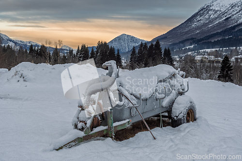 Image of Old machinery covered in snow sits in a winter field against a m