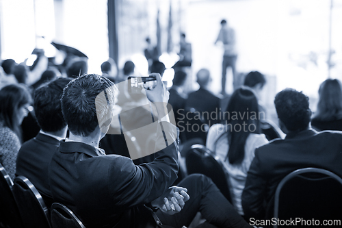 Image of Businessman takes a picture of corporate business presentation at conference hall using smartphone.