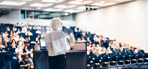 Image of Female speaker giving a talk on corporate business conference. Unrecognizable people in audience at conference hall. Business and Entrepreneurship event.