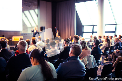 Image of Speaker giving a talk in conference hall at business event. Rear view of unrecognizable people in audience at the conference hall. Business and entrepreneurship concept.