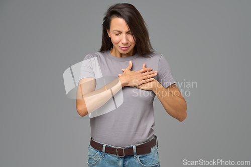 Image of Woman holding chest with both hands and eyes closed in discomfort, studio shot