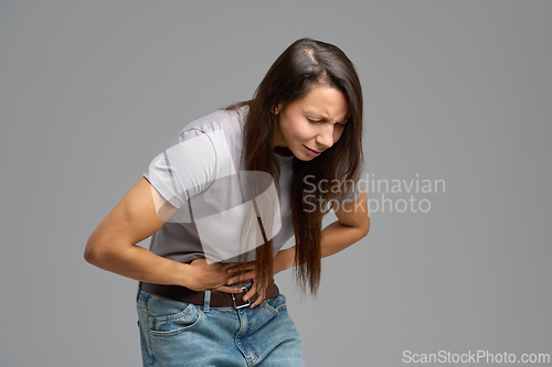 Image of Woman bending forward and holding abdomen in pain, studio scene on neutral grey