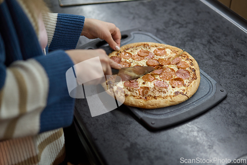 Image of Cutting pepperoni pizza on kitchen counter