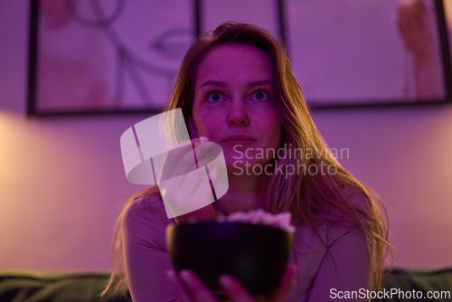 Image of Female watching screen with popcorn bowl on sofa indoors