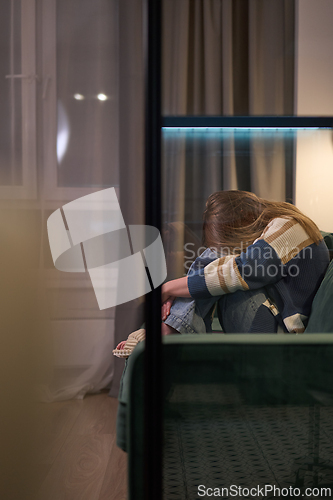 Image of Female curled up on sofa in dimly lit room