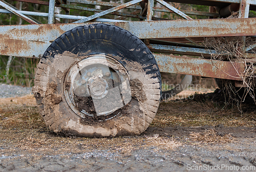 Image of Wheel of an old cart covered in mud rests on a gravel road in a 