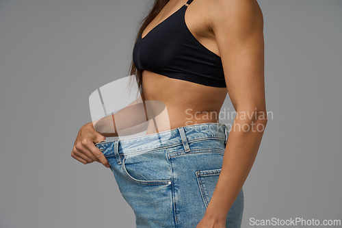 Image of Athletic woman in black sports bra and loose jeans demonstrating successful weight loss results