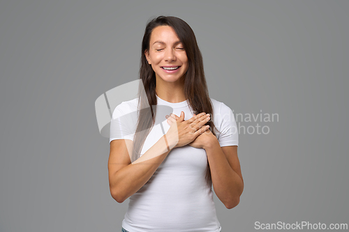Image of Smiling woman with eyes closed holding hands on chest expressing gratitude