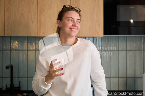 Image of Smiling Woman Holding a Glass in Warm Kitchen Light