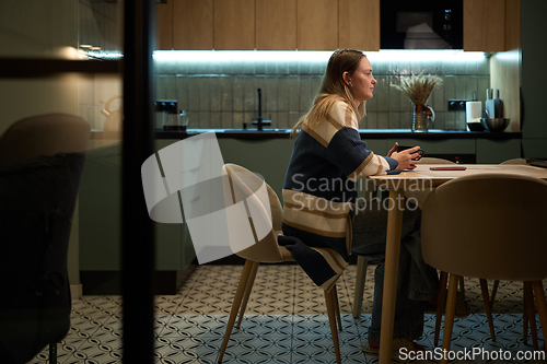Image of Woman sitting in profile at kitchen table with coffee mug