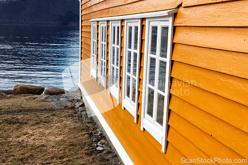 Image of Bright orange wooden cabin near calm waters reflects a serene la