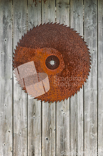 Image of Rusty metal saw blade hangs prominently against weathered wooden