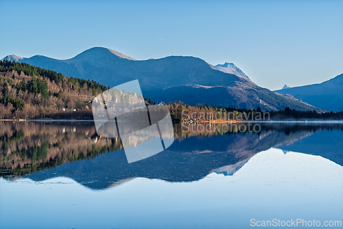 Image of Serene mountain landscape reflecting on calm waters during a cle