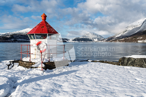 Image of Snow-covered lighthouse stands proudly by the calm waters of a f