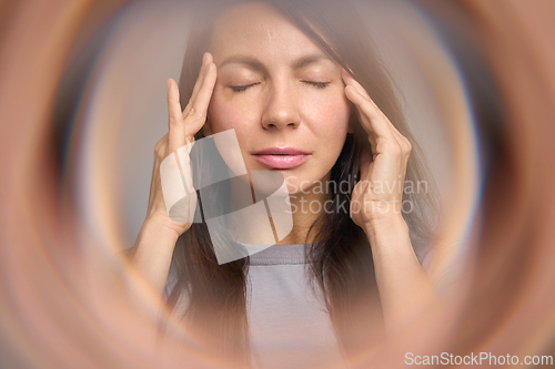 Image of Centered portrait of woman pressing temples inside circular bokeh. Eyes closed