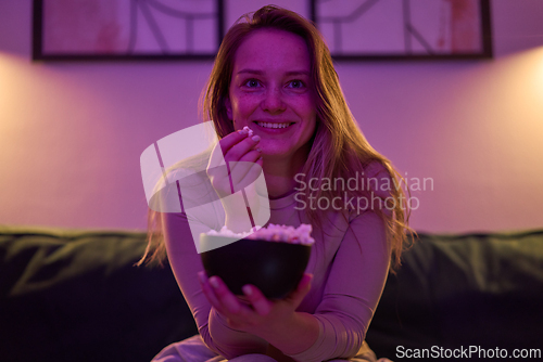 Image of Female seated indoors eating popcorn and watching screen