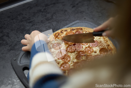 Image of Hands cutting pepperoni pizza on kitchen counter