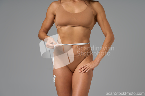 Image of Fit woman in sportswear measuring waistline with tape to track fitness