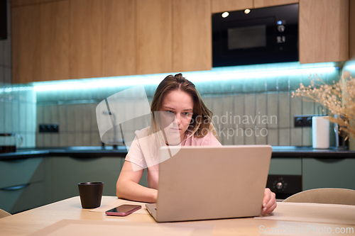 Image of Freelancer woman working on laptop at kitchen table with coffee cup