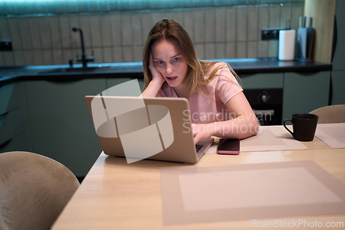 Image of Freelance woman reacting to laptop screen while working at kitchen table