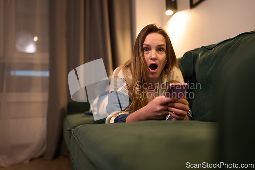 Image of Shocked reaction of woman looking at smartphone in cozy room