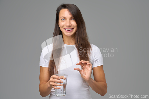 Image of Smiling woman holding glass of water and vitamin capsule representing