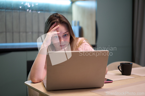 Image of Female concentrating on laptop at kitchen table indoors