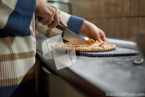 Image of Person slicing pepperoni pizza on kitchen counter