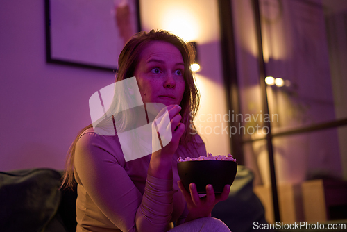 Image of Female eating popcorn while watching a screen in dim room