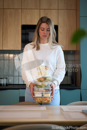 Image of Woman Carrying a Tall Stack of Meal Containers in Kitchen