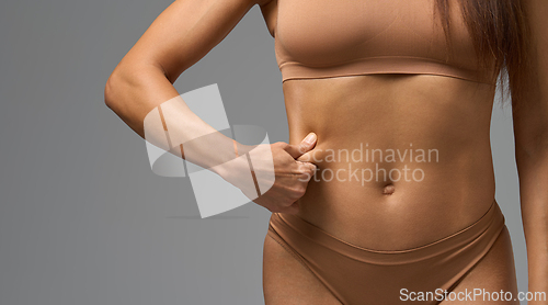 Image of Close-up of woman in beige underwear pinching skin on side of stomach in studio light.