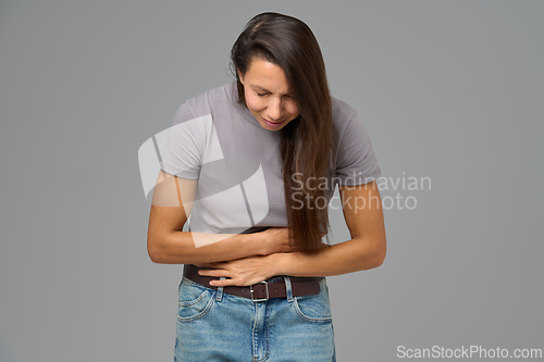 Image of Woman holding stomach and bending forward in discomfort, studio image on grey