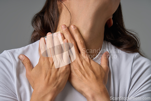 Image of Close-up of woman touching her neck with both hands showing pain and discomfort
