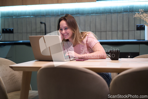 Image of Smiling female using laptop at kitchen table indoors