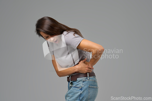 Image of Side view of woman with hand on lower back bending in pain, kidney pain
