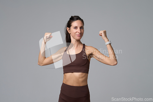 Image of Strong fit woman showing biceps muscles after workout in studio on grey background