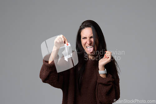 Image of Disgusted woman holding dirty tissue away from face with grimace isolated on grey background