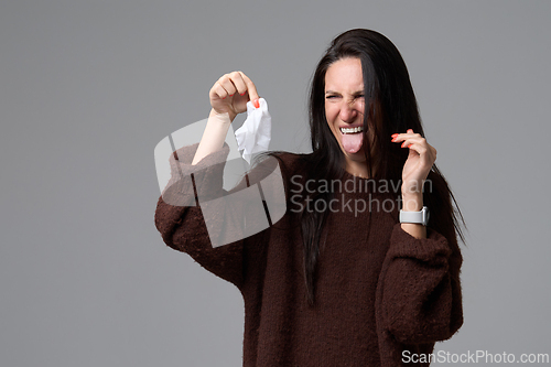 Image of Female sticking out tongue with disgusted face holding used paper tissue on grey background