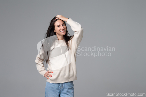 Image of Cheerful woman fixing hair with hand looking at camera on grey background