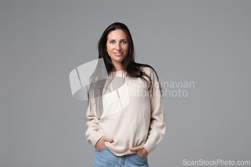 Image of Portrait of smiling woman in white sweater standing with hands in pockets on grey background